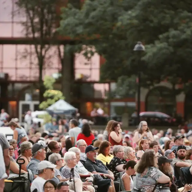 Large outdoor gathering of diverse people seated and standing in a park-like setting during daytime.
