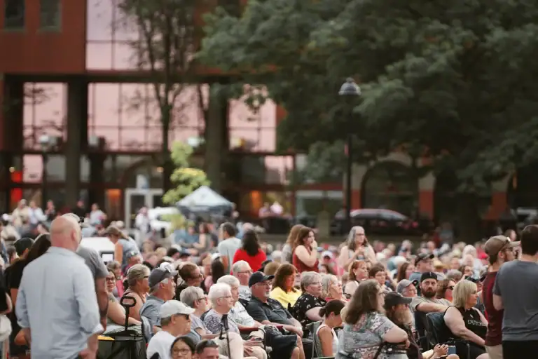 Large outdoor gathering of diverse people seated and standing in a park-like setting during daytime.