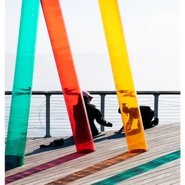 Brightly colored glass panels on a waterfront promenade with a person sitting in the background.