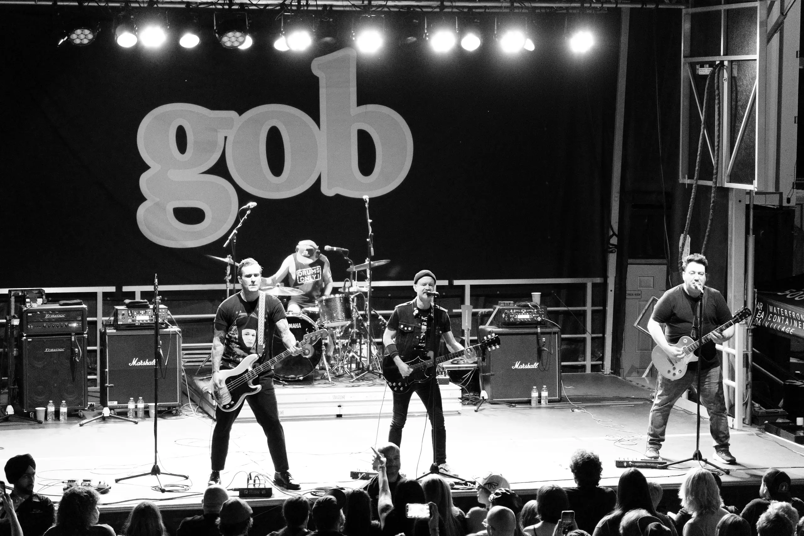 A four-member band performing live on stage with guitars and drums, with a large 'gob' sign in the background and an audience watching.