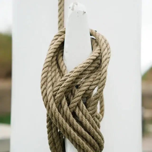 Close-up of a thick brown rope tied in a knot around a white post, outdoors with a blurred background.