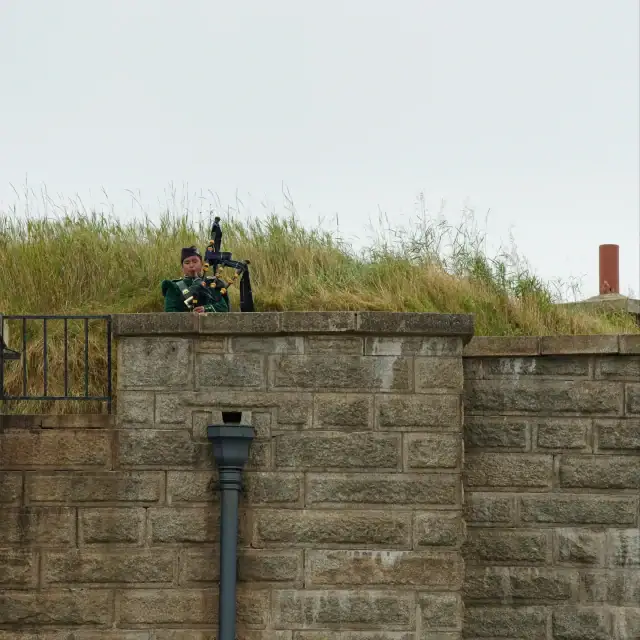 Security guard sitting on a stone wall with a grassy area and cloudy sky in the background.