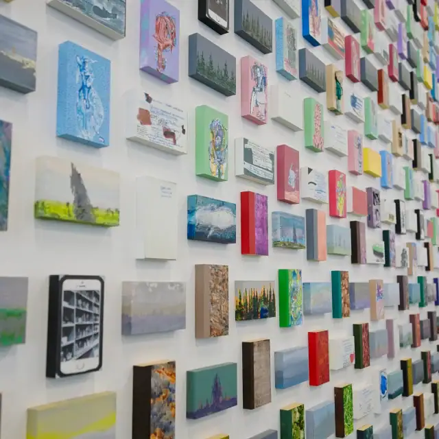 A vibrant wall filled with numerous small, colorful paintings and artworks arranged in a grid pattern.