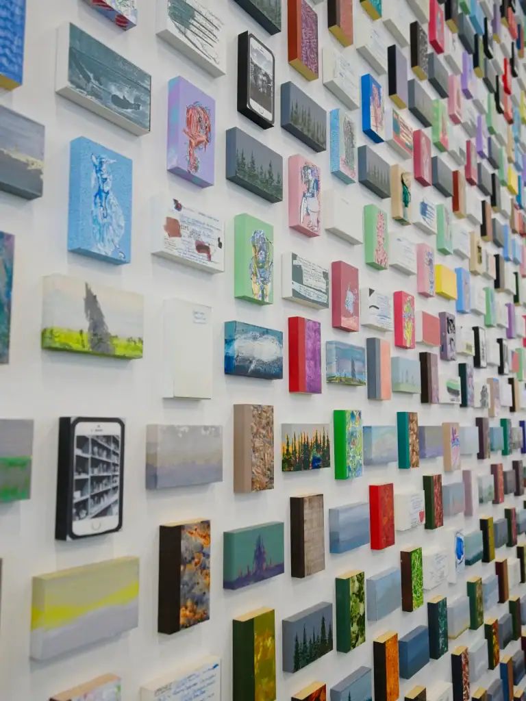 A vibrant wall filled with numerous small, colorful paintings and artworks arranged in a grid pattern.