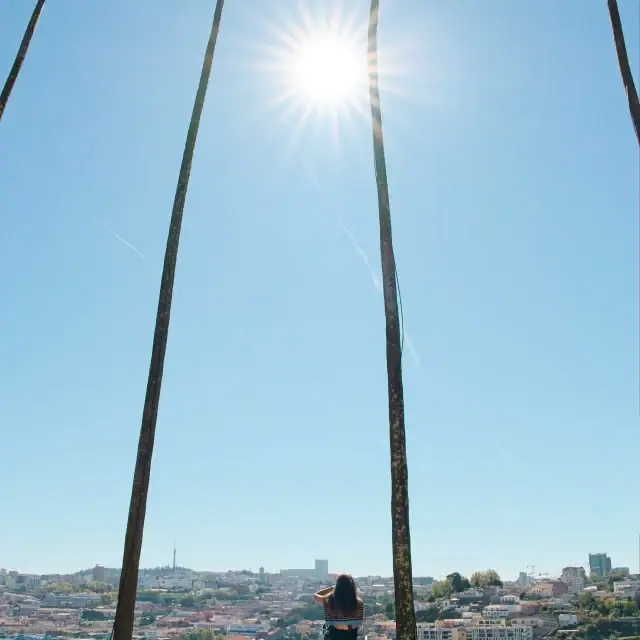 A person standing on a sunny beach under tall palm trees, with a bright sun overhead and a coastal town in the distance.
